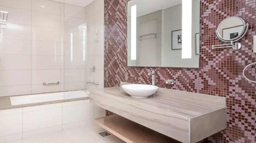 Salle de bains moderne dans les tours Damac avec carreaux de mosaïque rouge, vanité flottante en bois avec lavabo blanc et grand miroir au-dessus. Le sol est carrelé et il y a une cabine de douche en verre au