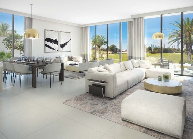 Un salon spacieux et moderne à Dubai Hills avec un grand canapé blanc, des portes vitrées menant à une pelouse et un coin repas avec une table dressée, sous une lumière naturelle vive.