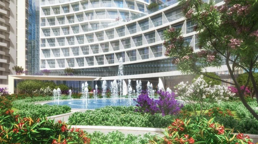 Un jardin luxuriant avec des fleurs colorées et une fontaine devant un bâtiment moderne en verre incurvé, mettant en valeur une oasis urbaine à Seven Palm.