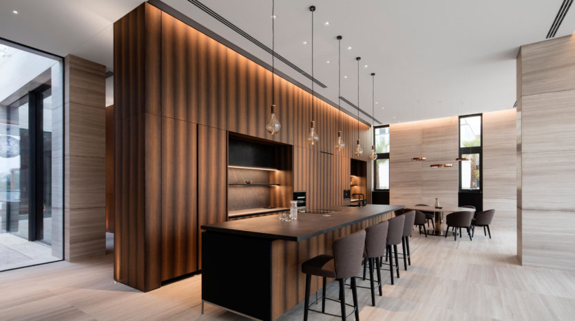 Intérieur de cuisine moderne à Dubai Hills avec des boiseries élégantes, un comptoir noir intégré et des tabourets de bar, avec un éclairage suspendu et de grandes fenêtres.