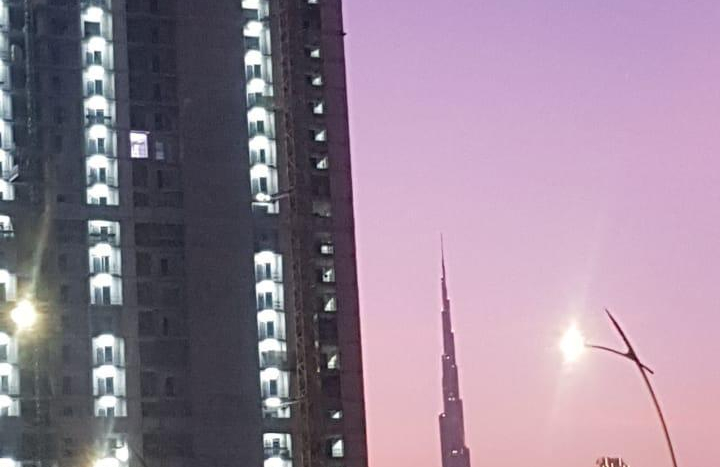 Une scène crépusculaire avec un ciel rose, mettant en vedette une grue de construction au sommet d&#039;un immeuble de grande hauteur en construction et la silhouette du Burj Khalifa au loin à Creek Vistas, Dubaï.