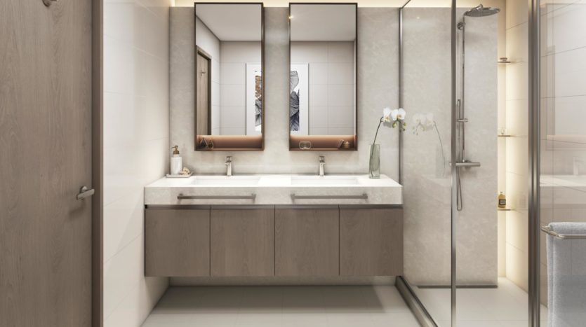 Une salle de bains moderne dotée d&#039;une double vasque avec de grands miroirs, de meubles sous l&#039;évier et d&#039;un espace douche aux parois de verre. Les tons neutres et les lignes épurées dominent le design chez Elie Saab Emaar