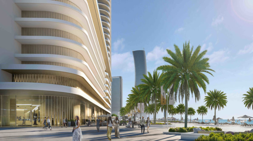 Un immeuble de grande hauteur moderne et curviligne à côté d&#039;une promenade bordée de palmiers remplie de piétons sous un ciel bleu clair sur le front de mer d&#039;Elie Saab Emaar.