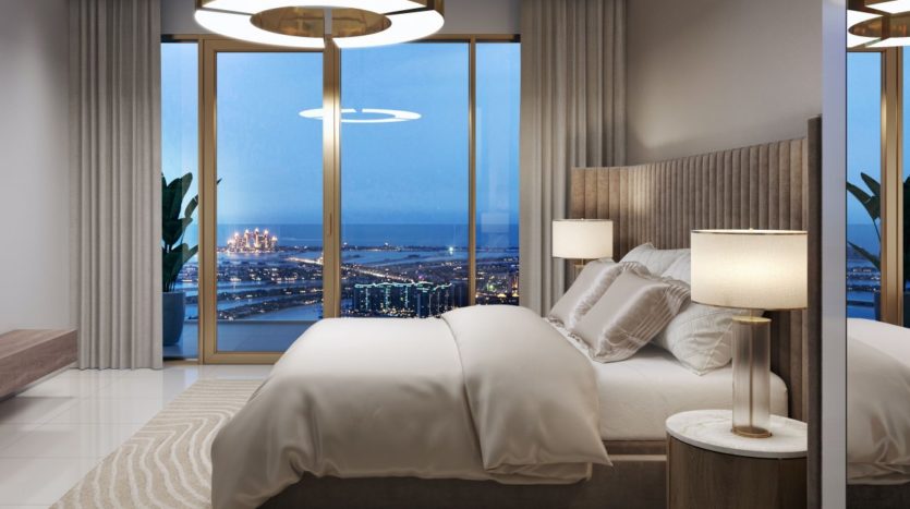Une chambre luxueuse la nuit avec un grand lit, des lampes élégantes et des baies vitrées donnant sur le paysage urbain et l&#039;océan bien éclairés du front de mer d&#039;Elie Saab Emaar.