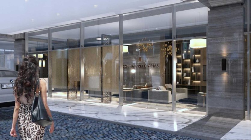 Une femme s'approche de l'entrée en verre moderne d'un bâtiment sophistiqué avec un éclairage intérieur élégant et un design chic, affichant bien en évidence une pancarte indiquant "Creek Vistas Dubai".