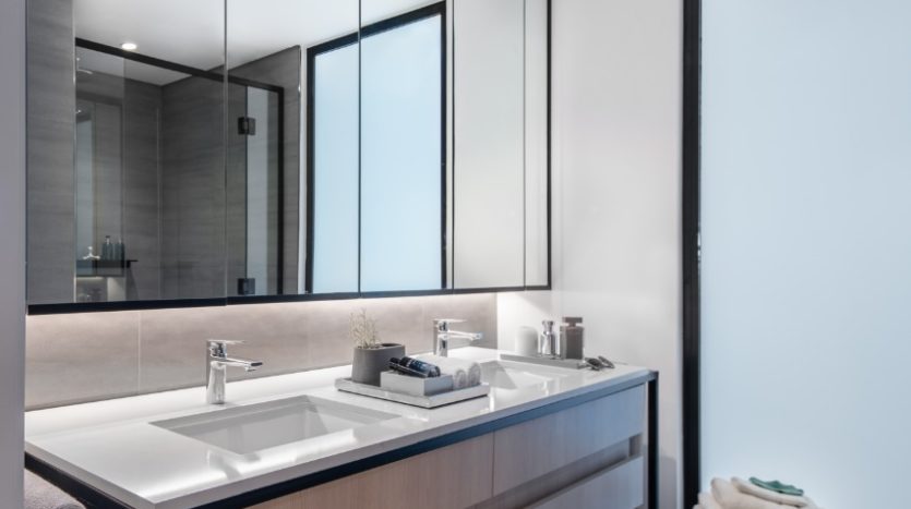 Une salle de bains moderne à Wilton Park comprenant un grand miroir au-dessus d&#039;un meuble-lavabo à double lavabo avec rangement sous l&#039;armoire. Les tons neutres avec des cadres noirs contrastés sont évidents, mettant en valeur un design minimaliste avec un éclairage lumineux.