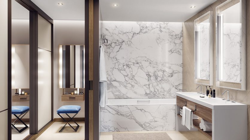 Une salle de bains moderne de l'Address Residences Dubai Opera avec des murs en marbre blanc, comprenant un meuble-lavabo à double vasque, de grands miroirs, une baignoire intégrée, des chaises bleues et un éclairage d'ambiance.