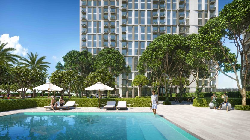 Une vue panoramique sur la piscine d&#039;un hôtel de luxe avec des clients se relaxant sur des chaises longues, entourés d&#039;une verdure luxuriante et le bâtiment moderne Collective 2.0 Dubai Hills en arrière-plan.