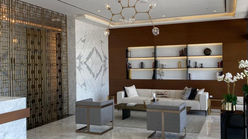 Hall d&#039;entrée moderne avec sols en marbre, comptoir de réception en bois, coin salon élégant, éclairage décoratif et orchidées blanches. Les couleurs neutres et la décoration élégante contribuent à une atmosphère sereine offrant une vue imprenable sur Dubaï.