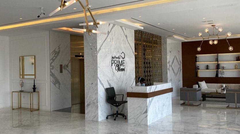 Lobby d&#039;hôtel moderne doté d&#039;un sol et d&#039;un bureau en marbre, de touches dorées sur le mobilier et d&#039;un éclairage décoratif offrant une vue imprenable sur Dubaï. Une réceptionniste travaille au bureau.