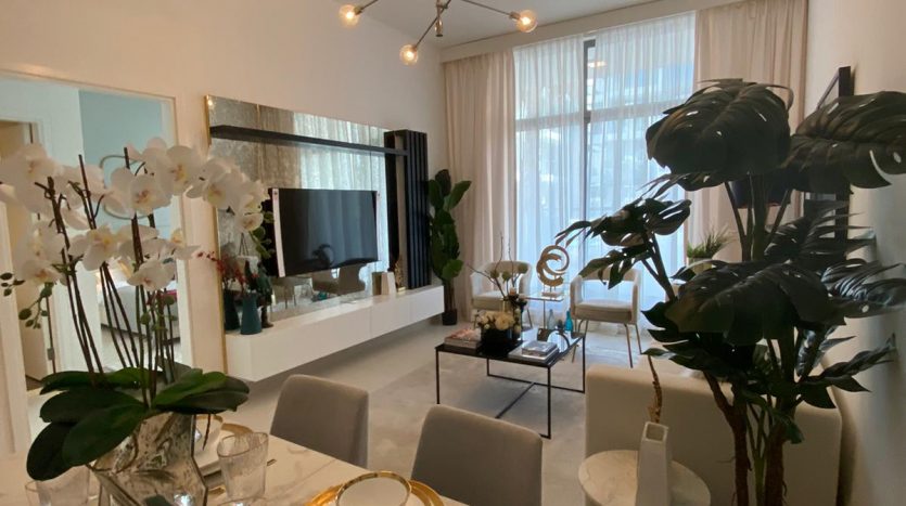Une salle à manger moderne avec une table en marbre blanc pour quatre personnes, offrant une vue imprenable sur Dubaï. Un lustre élégant est suspendu au-dessus et la pièce comprend une grande plante en pot, un décor blanc et