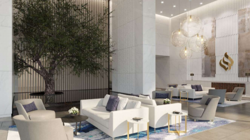 Hall d&#039;entrée moderne du Jumeirah Living Marina Gate avec canapés blancs et gris, chaises élégantes et tables basses centrales. Des suspensions élégantes sont suspendues au-dessus et un grand arbre intérieur ajoute une touche d&#039;ambiance.