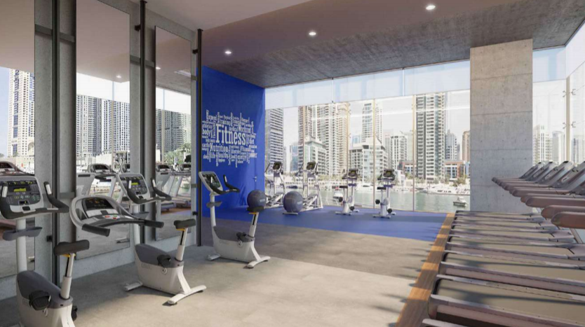 Salle de sport moderne du Jumeirah Living Marina Gate surplombant le front de mer de la ville, équipée de tapis roulants et de diverses machines de cardio, dotée de grandes fenêtres et d&#039;un aménagement spacieux.