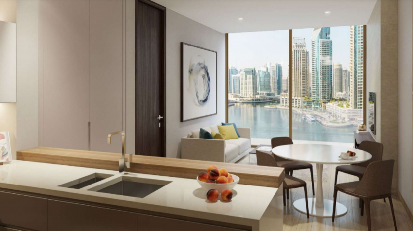 Cuisine et salon modernes donnant sur Jumeirah Living Marina Gate, avec une grande fenêtre, un bol de fruits sur le comptoir et un coin repas confortable.