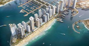 Vue aérienne d'un développement urbain côtier avec des gratte-ciel près d'une marina remplie de bateaux, à côté d'une plage de sable aux eaux turquoise claires.