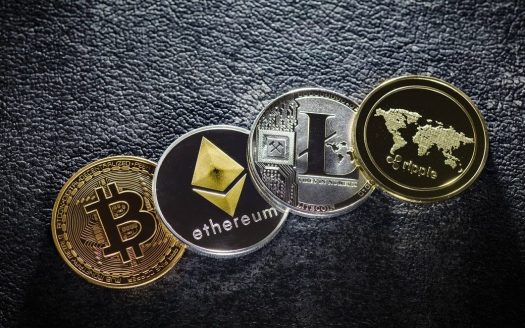 Quatre types différents de pièces de crypto-monnaie, dont Bitcoin, Ethereum, Litecoin et une autre, disposés sur une surface sombre texturée pour symboliser l'utilisation du Bitcoin pour acheter un appartement à Dubaï.