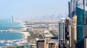 El horizonte de Dubai, con modernos rascacielos, el Burj Al Arab y vistas de la costa y el puerto, ideal para quienes buscan invertir en propiedades, bajo un cielo azul despejado.