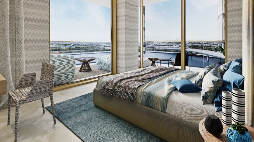 Chambre moderne avec un grand lit, des textiles à motifs Missoni et des baies vitrées donnant sur une rivière. Le décor comprend une chaise rayée et une table ronde, avec de la lumière naturelle remplissant le
