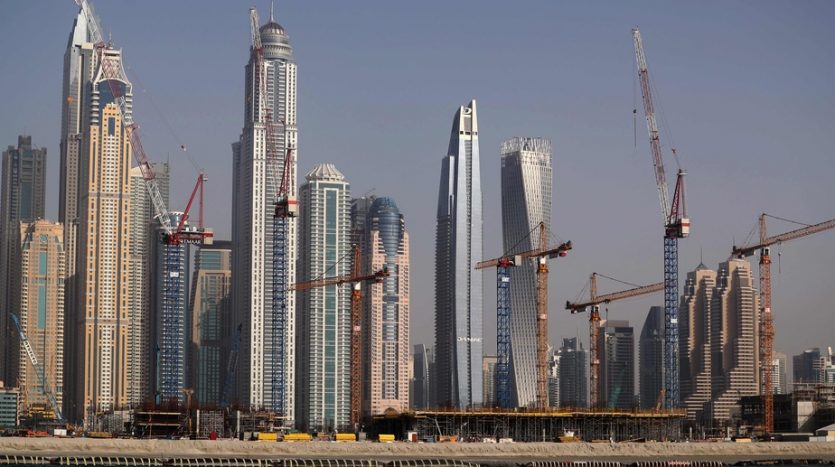 Horizon de gratte-ciel modernes en construction par un promoteur immobilier à Dubaï avec plusieurs grues, sur un ciel bleu clair et vu de l&#039;autre côté de l&#039;eau.