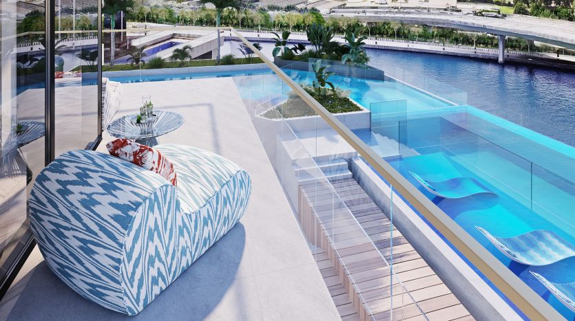 Luxueux toit-terrasse avec une piscine à débordement transparente surplombant une rivière sereine, équipé d&#039;élégants poufs à rayures bleues et blanches de Missoni et d&#039;un coin repas soigneusement aménagé.