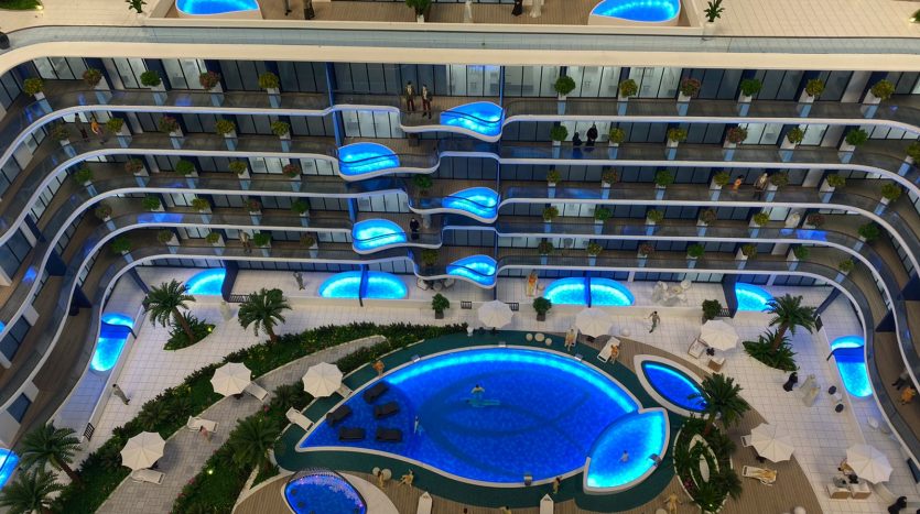Vue aérienne d&#039;un atrium d&#039;hôtel comprenant une piscine bleu vif en forme de rein entourée de palmiers, de coins salons et de balcons d&#039;hôtel à plusieurs étages éclairés d&#039;accents bleus, offrant un vaste Samana
