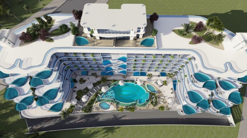 Vue aérienne d'un complexe de luxe au design ondulé bleu unique, comprenant une piscine centrale entourée de salons couverts de parasols, flanquée d'ailes de bâtiment symétriques donnant sur les vues du parc Samana.