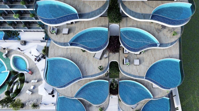 Vue aérienne de Samana Park Views, un immeuble d&#039;appartements moderne avec des piscines uniques en forme de larme sur chaque balcon, entremêlées de terrasses blanches et en bois.