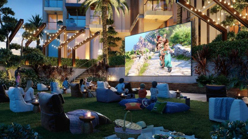 Soirée cinéma en plein air dans un jardin joliment éclairé, avec des gens assis sur diverses chaises et coussins regardant un grand écran diffusant un film d&#039;animation. Cet événement a lieu au regalia Dubai, entouré d&#039;une végétation luxuriante