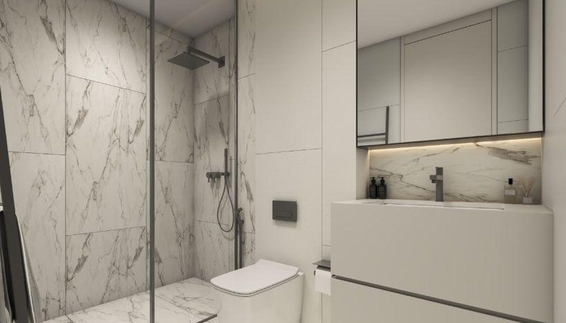 Une salle de bains moderne avec des murs et des sols en marbre, comprenant une douche en verre, des toilettes blanches et une vasque avec un grand miroir éclairé par des plafonniers à Regalia Dubai.