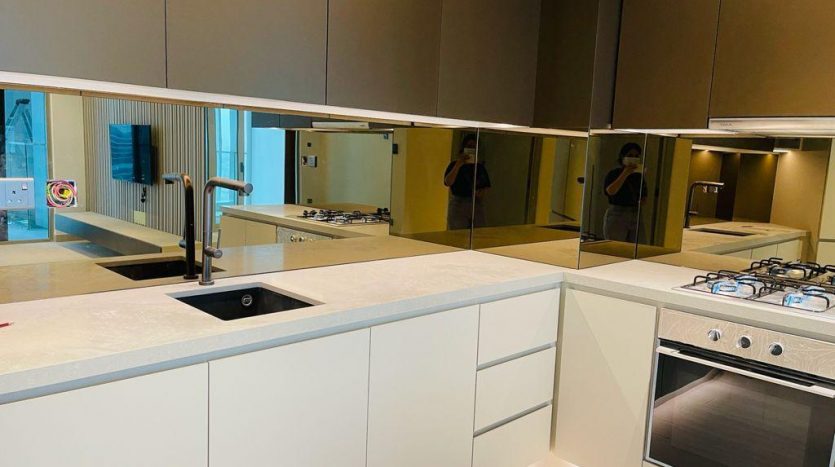 Une cuisine moderne avec des armoires blanches, des appareils électroménagers intégrés et un évier noir. Le dosseret en miroir Regalia Dubai reflète la pièce et la personne qui prend la photo.