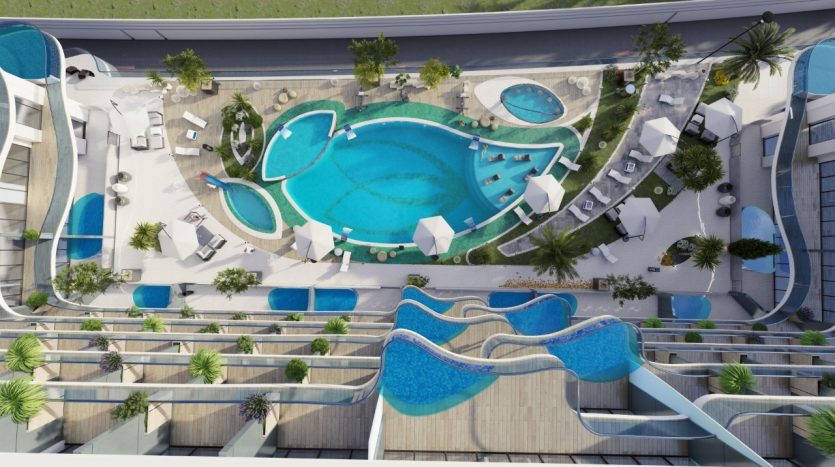 Vue aérienne d'une piscine de luxe avec une grande piscine bleue, des piscines plus petites, des chaises longues blanches, une vue sur le parc Samana et les bâtiments environnants.
