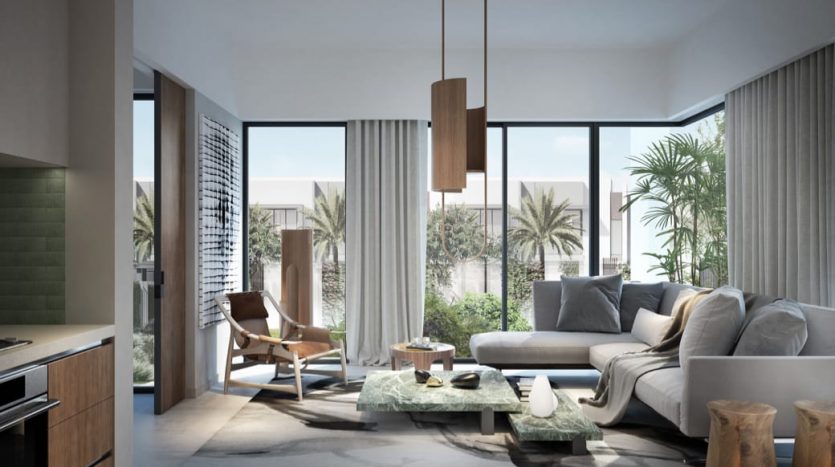 Intérieur de salon moderne avec un canapé gris, des chaises en bois, une table centrale et de grandes fenêtres donnant sur un espace extérieur bordé de palmiers dans la Valley Dubai. La lumière naturelle remplit l&#039;espace, renforçant le calme
