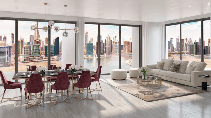 Salon moderne avec un canapé beige, des chaises rouges et une table en verre, donnant sur les toits de la grande ville de The Peninsula Dubai à travers des baies vitrées. Ambiance lumineuse et aérée.