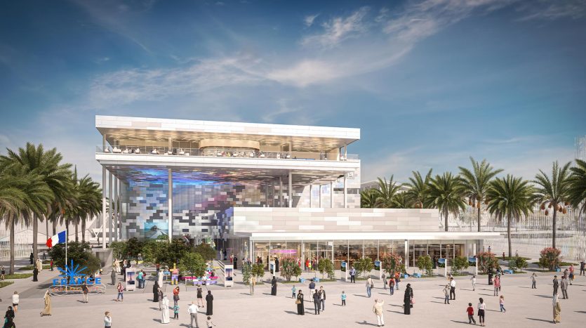 Un bâtiment moderne de plusieurs étages avec une façade en verre et des écrans numériques vibrants, entouré de palmiers et d&#039;une place animée avec divers groupes de personnes, stratégiquement situé à proximité du site de Dubai Expo 2020.