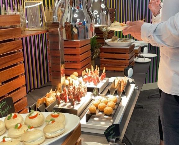 Une personne se sert à un buffet moderne proposant une gamme d&#039;entrées, avec des ustensiles en acier et un fond rayé coloré lors de l&#039;Expo de Dubaï 2020.