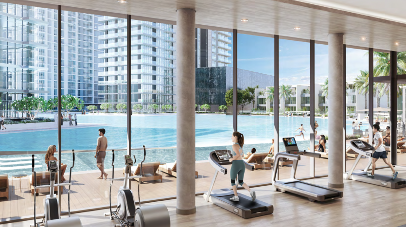 Une salle de sport moderne dotée de baies vitrées donnant sur un front de mer serein à Dubaï. Les gens utilisent des tapis roulants et des vélos elliptiques, et une verdure luxuriante entoure les immeubles de grande hauteur à proximité.