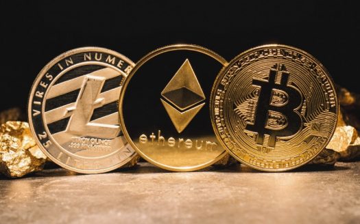 Trois pièces de crypto-monnaie – Litecoin, Ethereum et Bitcoin – se dressent debout sur fond de pépites d'or à Dubaï, éclairées par une lumière chaude et dorée.