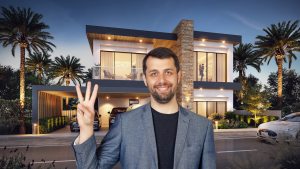 Un homme souriant avec une barbe, faisant un signe de paix, se tient devant une maison moderne à deux étages à Dubaï avec des intérieurs éclairés, des palmiers et une voiture garée à l'extérieur au crépuscule.