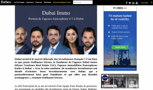 Image montrant cinq professionnels, trois hommes et deux femmes, vêtus d'une tenue professionnelle, posant pour une photo de groupe pour Forbes. Leurs expressions sont sérieuses et ils se tiennent devant un paysage urbain flou.