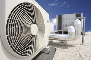 Une grande unité de climatisation industrielle dotée d'un ventilateur circulaire proéminent, positionnée sur le toit d'un immeuble à Dubaï sous un ciel bleu clair.
