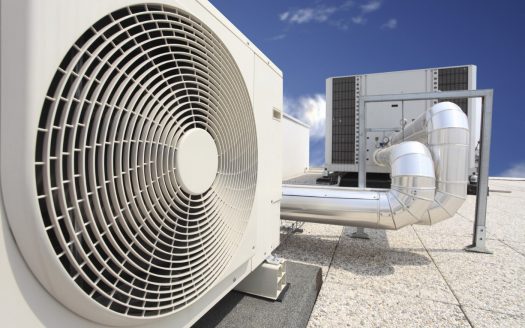 Une grande unité de climatisation industrielle dotée d'un ventilateur circulaire proéminent, positionnée sur le toit d'un immeuble à Dubaï sous un ciel bleu clair.