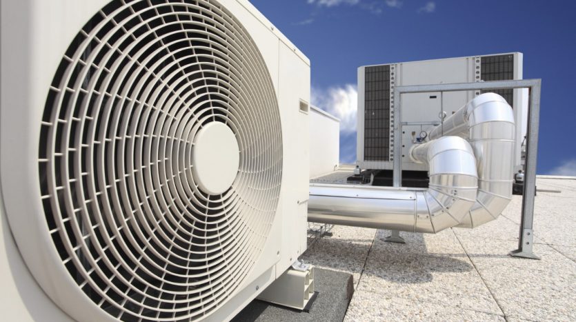 Une grande unité de climatisation industrielle dotée d&#039;un ventilateur circulaire proéminent, positionnée sur le toit d&#039;un immeuble à Dubaï sous un ciel bleu clair.