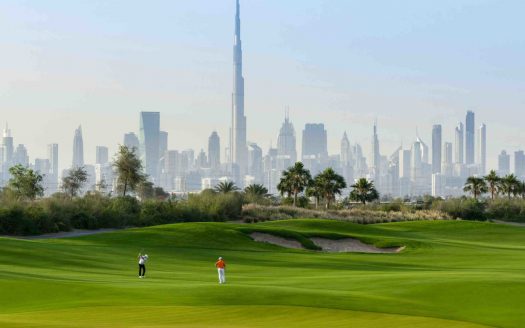 Deux golfeurs sur un parcours vert vif avec un bunker de sable, mettant en avant une vue panoramique sur les toits de Dubaï, y compris le Burj Khalifa, situé dans l'un des meilleurs quartiers de Dubaï.