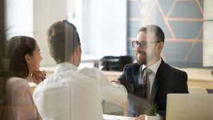 Trois professionnels, une femme et deux hommes, engagent une conversation sur le financement bancaire dans un bureau moderne avec des ordinateurs portables visibles sur la table.