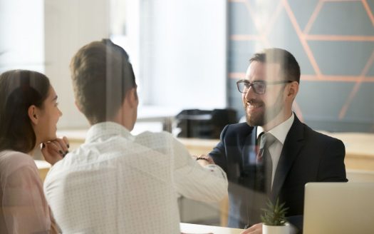 Trois professionnels, une femme et deux hommes, engagent une conversation sur le financement bancaire dans un bureau moderne avec des ordinateurs portables visibles sur la table.