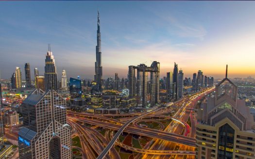 Vue grand angle de Dubaï au coucher du soleil, mettant en vedette le Burj Khalifa et les gratte-ciel environnants avec des rues illuminées et des routes très fréquentées, présentant le meilleur investissement à Dubaï.