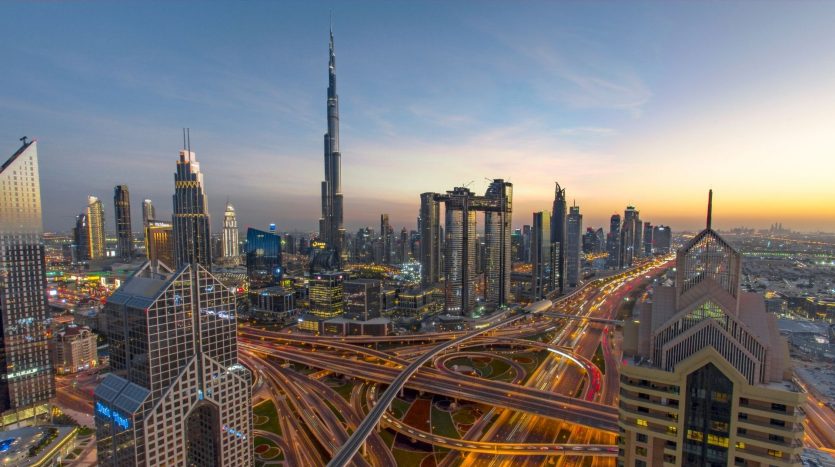 Vue grand angle de Dubaï au coucher du soleil, mettant en vedette le Burj Khalifa et les gratte-ciel environnants avec des rues illuminées et des routes très fréquentées, présentant le meilleur investissement à Dubaï.