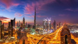 Vue panoramique sur les toits d'une ville animée au crépuscule avec des gratte-ciels illuminés et des autoroutes très fréquentées, avec une haute tour proéminente parmi l'architecture de la ville, mise en valeur par la taxe immobilière unique de Dubaï