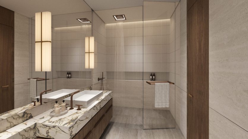Une salle de bains moderne et spacieuse avec des comptoirs en marbre, des meubles-lavabos en bois et une décoration minimaliste. La pièce dispose de grands miroirs et d&#039;un éclairage subtil de Six Senses, créant une atmosphère élégante.
