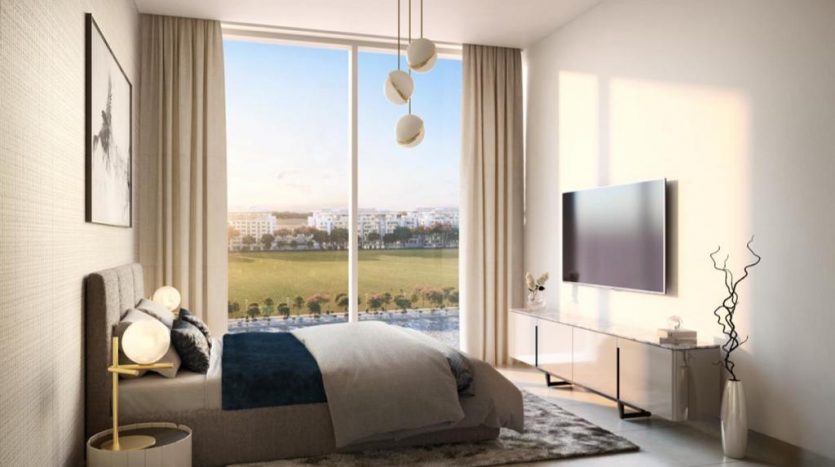 Une chambre confortable et moderne à The Crest Dubai comprenant une grande fenêtre avec une vue panoramique, un lit, une télévision et des éléments décoratifs comme un vase et des suspensions. La lumière du soleil remplit la pièce.